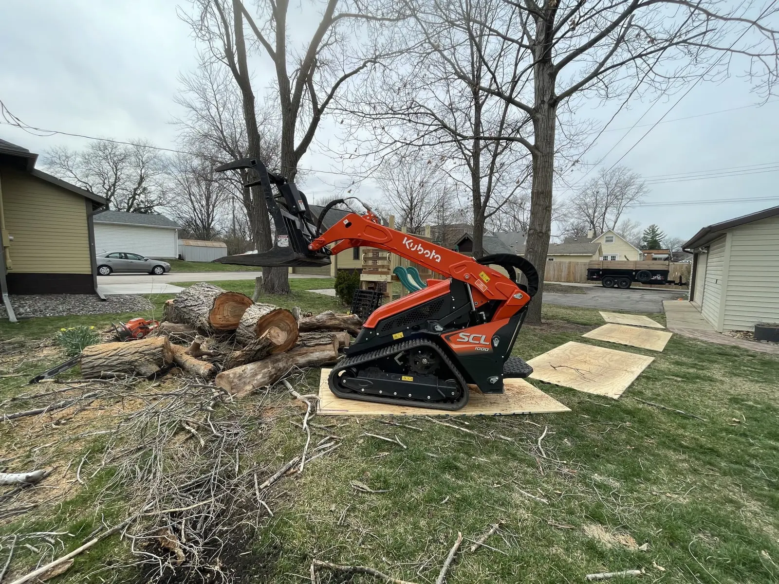 Rooted's mini skid steer on plywood mats beside a pile of cut logs